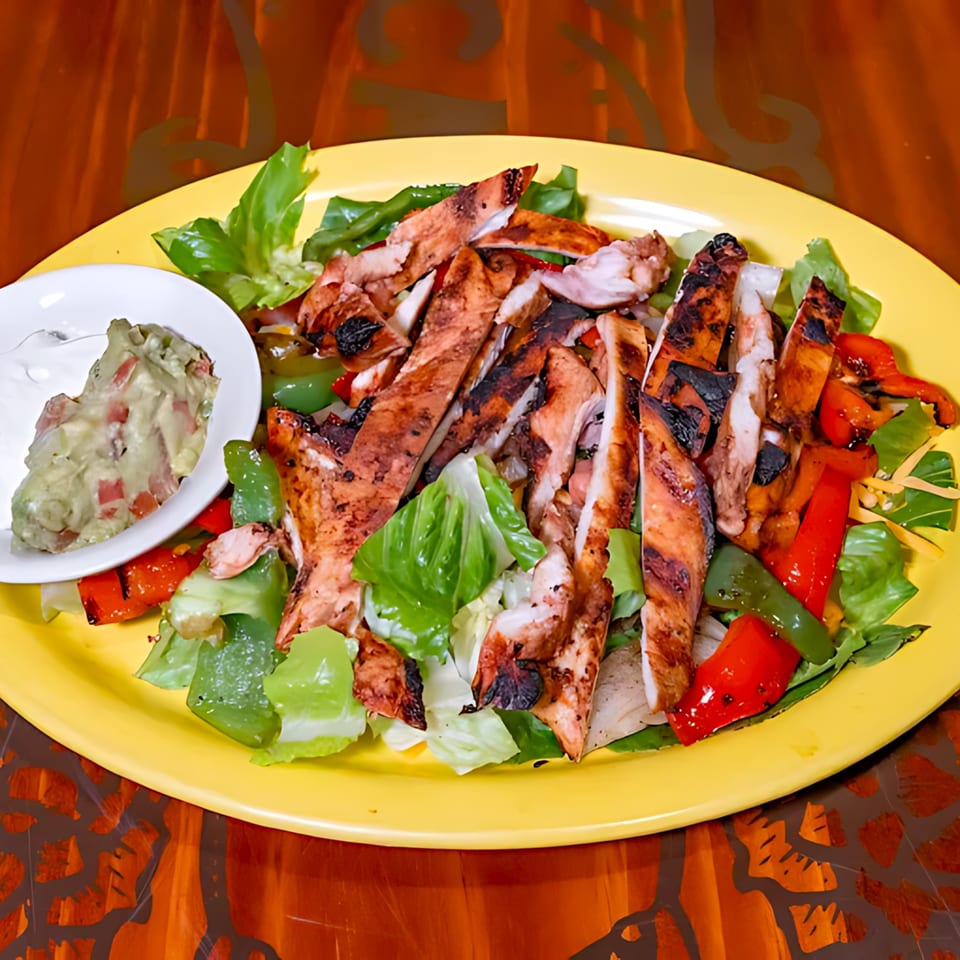 Grilled chicken fajita salad with bell peppers, lettuce, and a side of guacamole and sour cream.
