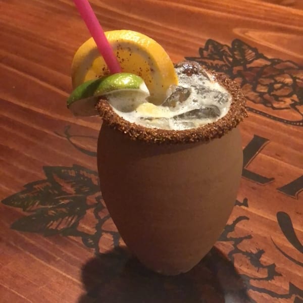 A Casa Vallarta cantarito cocktail, garnished with lime and orange, on a wooden table.