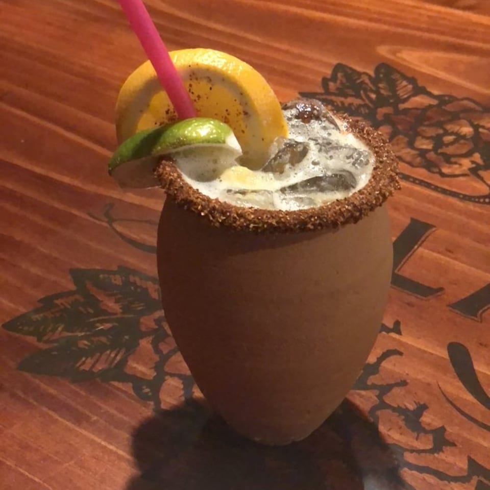 A Casa Vallarta cantarito cocktail, garnished with lime and orange, on a wooden table.
