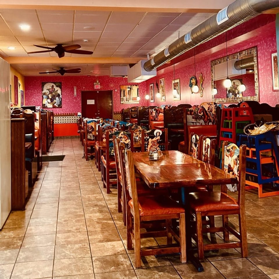 Interior of Casa Vallarta with pink walls, tiled floors, wooden tables, and chairs with colorful Mexican art.