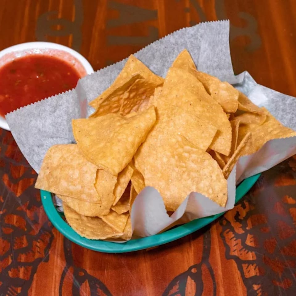 A basket of Casa Vallarta tortilla chips with a side of red salsa on a wooden table.
