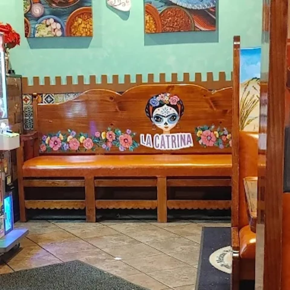Wooden booth seating with "La Catrina" painted on the back, adorned with colorful flowers.