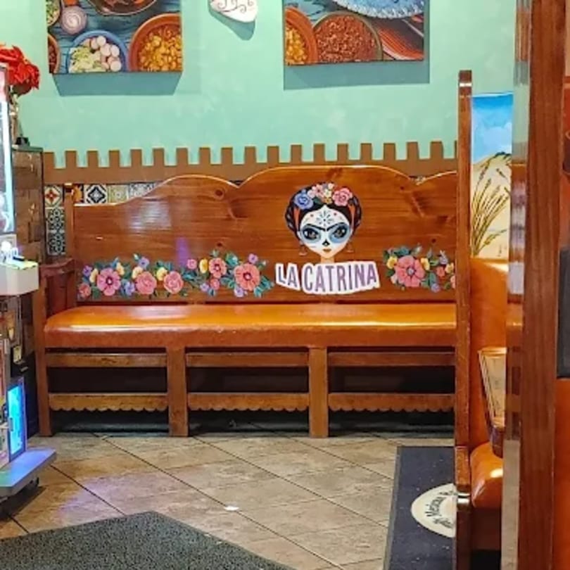Wooden booth seating with "La Catrina" painted on the back, adorned with colorful flowers.