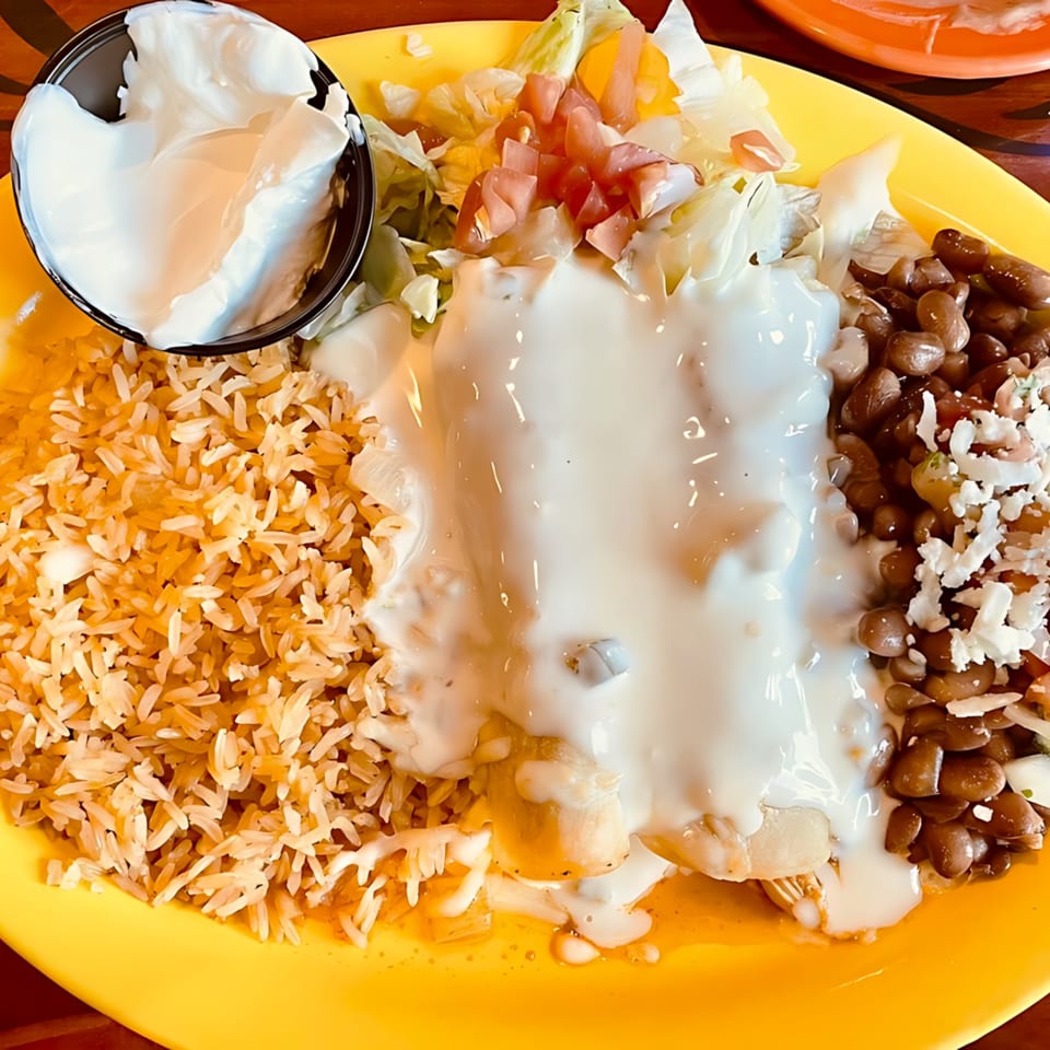 Casa Vallarta's chicken enchiladas with rice, beans, lettuce, tomatoes, and sour cream on a yellow plate.