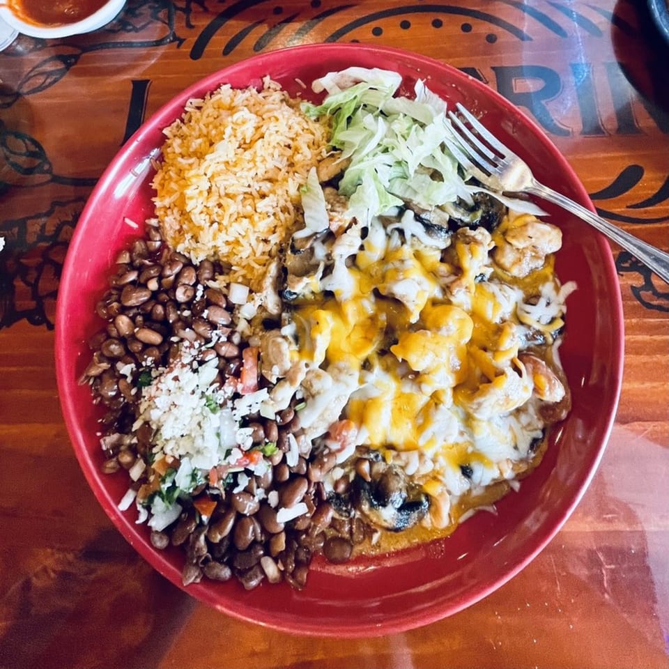 A vibrant red plate of Casa Vallarta's Mexican food with rice, beans, and cheesy chicken.