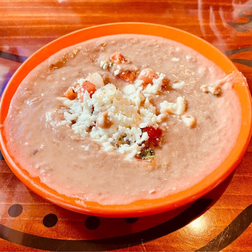 A bowl of refried beans topped with crumbled white cheese and diced tomatoes from Casa Vallarta.