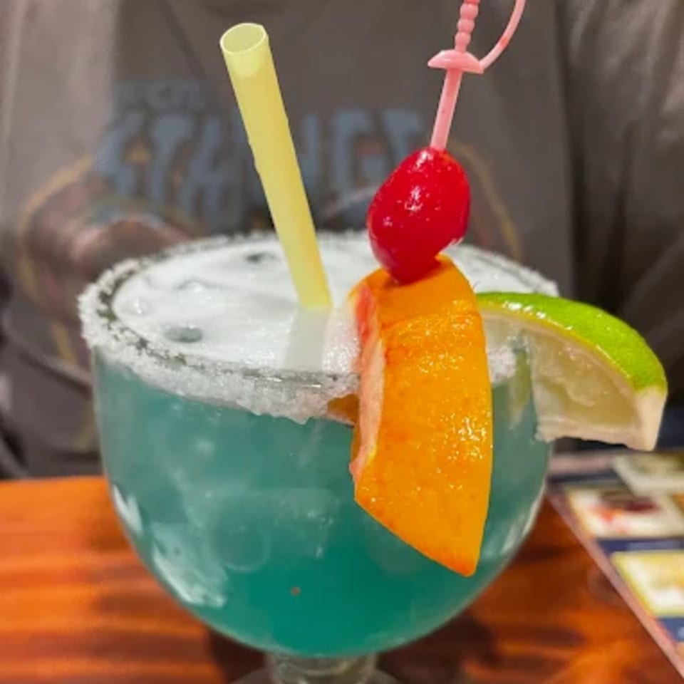 A vibrant blue margarita with a salted rim, garnished with an orange slice, lime, and cherry.
