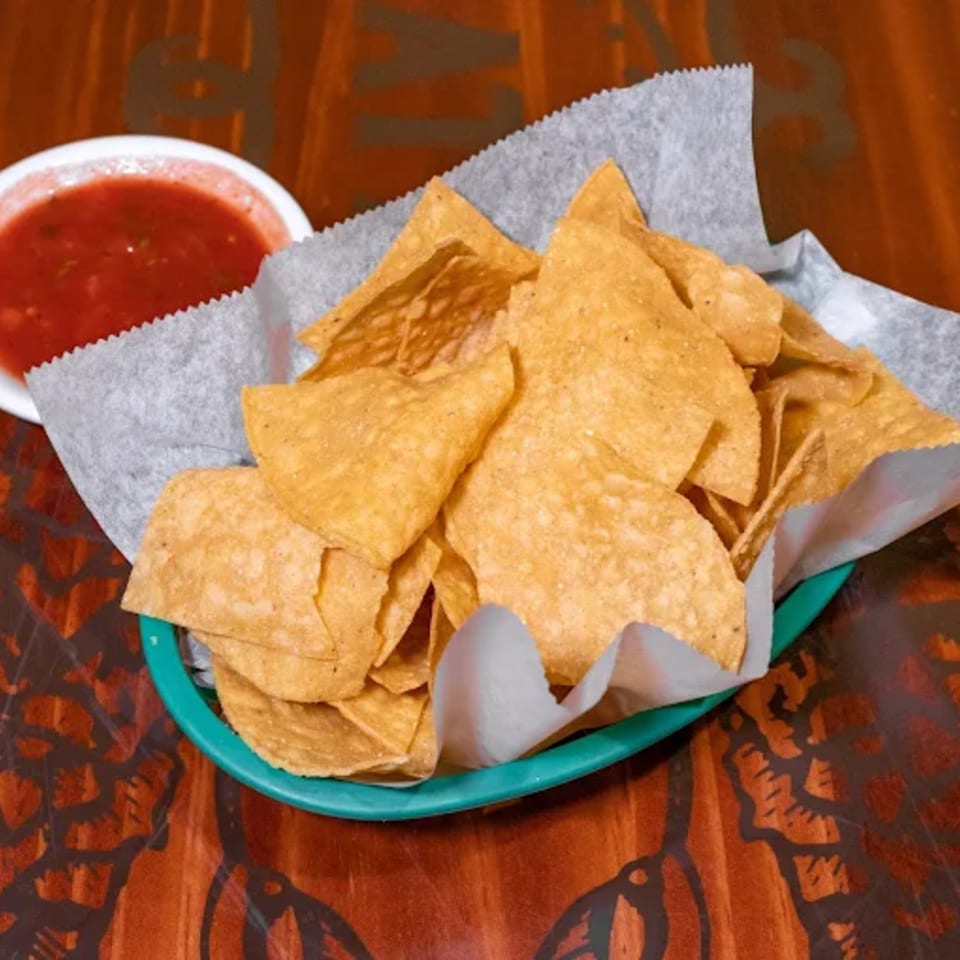 A basket of tortilla chips with a side of red salsa on a wooden table at Casa Vallarta.