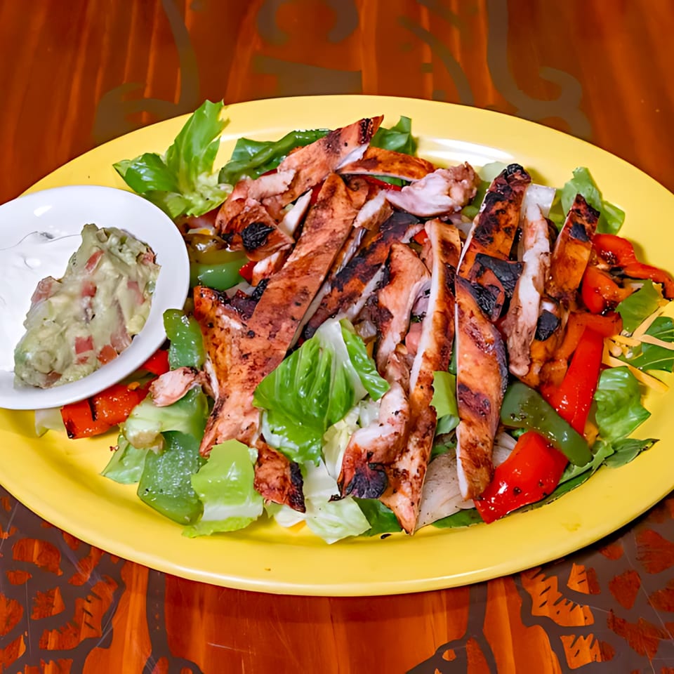 Casa Vallarta's grilled chicken fajita salad with bell peppers, lettuce, and a side of guacamole and sour cream.